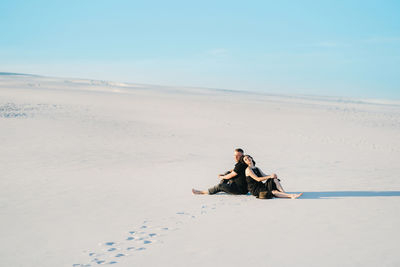 Men sitting on beach against sky