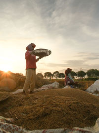 Farmers working at farm against sky during sunset