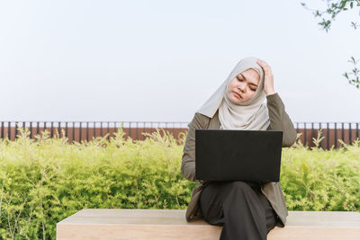 Full length of young woman using mobile phone against sky