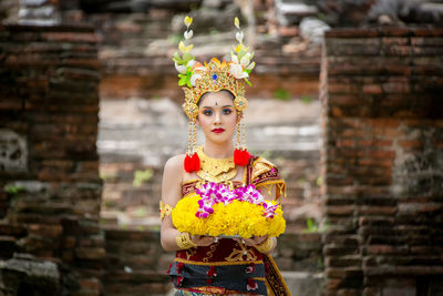 Portrait of young woman in traditional clothing holding flowers at temple