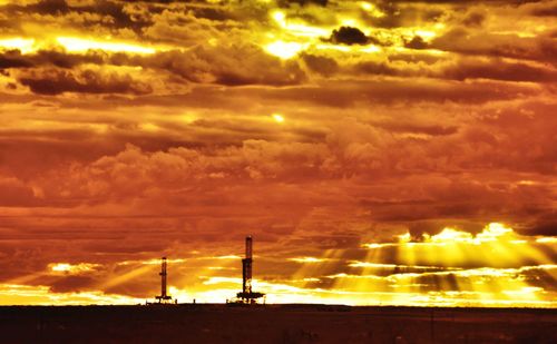 Silhouette of factory against dramatic sky during sunset