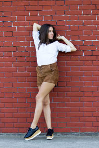 Portrait of young woman standing against brick wall