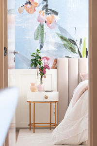 Interior of bedroom with floral ornament on wall with comfortable bed under blanket placed near round bedside table with vase of fresh plants