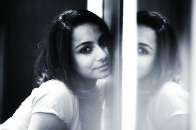 Portrait of young woman leaning on glass window at home