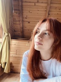 Portrait of young woman looking away while sitting on wood