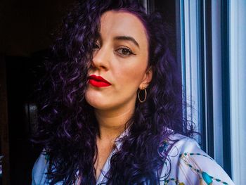 Portrait of smiling young woman standing by window at home