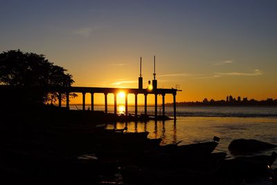 Silhouette built structure in calm sea at sunset