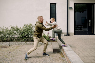 Full length of father catching son jumping at back yard