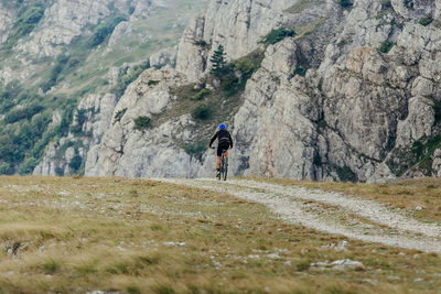Rear view of man cycling on land against mountain