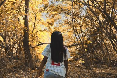 Rear view of woman standing amidst trees during autumn