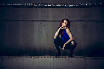 Portrait of young woman crouching against wall at parking lot