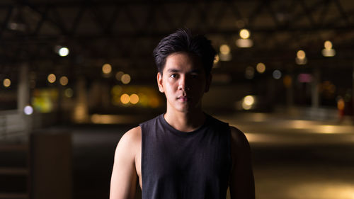 Portrait of young man standing against illuminated city at night