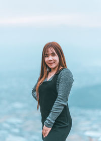 Portrait of smiling young woman standing against sea