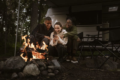 Friends sitting by campfire and using phone