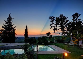 Silhouette trees by swimming pool against sky at sunset