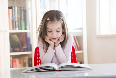 Portrait of little girl at table reading a book