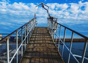 Wooden pier over sea against cloudy sky