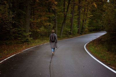 Rear view of man walking on road amidst trees