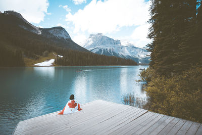 Woman with canada flag sitting on pier by river