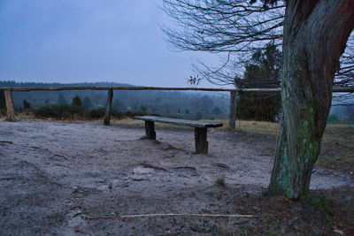 Empty bench on field by trees against sky