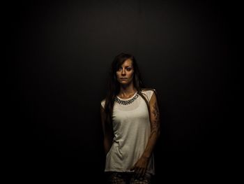 Tattooed young woman with long hair standing against black background