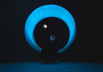 Man sitting at circular window against sky in darkroom