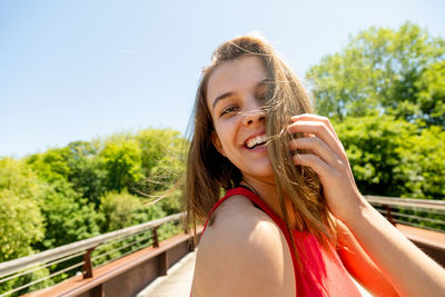 Portrait of beautiful smiling girl standing on footbridge against trees