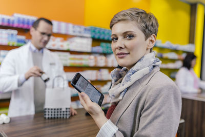 Portrait of woman with cell phone at counter in pharmacy