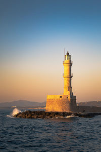 Chania lighthouse view at sunset golden light in the venetian harbour and a wave hitting the cliff 