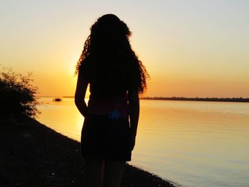 Rear view of woman standing on beach against sky during sunset