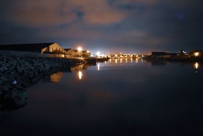 Illuminated buildings by sea against sky at night