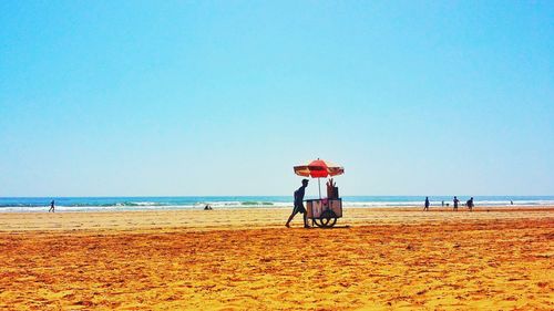 People on beach against clear blue sky