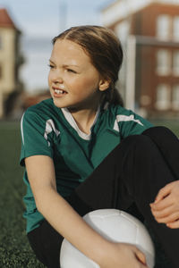Elementary girl with soccer ball day dreaming while sitting at sports field