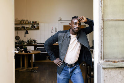 Portrait of businessman with hand on hip leaning at doorway of workshop