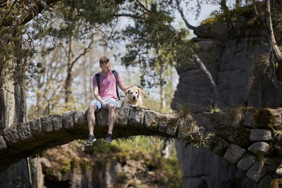 Man with his dog sitting old stone bridge. tourist with labrador resting in nature.