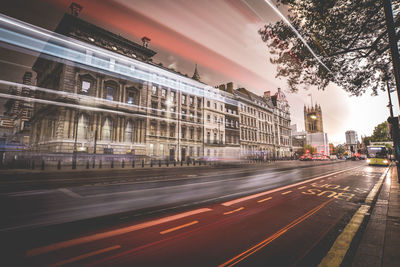 Light trails on road by buildings in city against sky