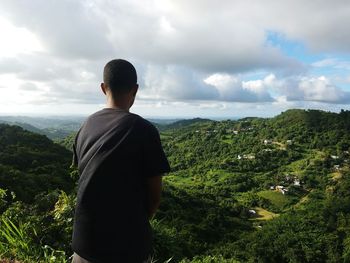 Rear view of man standing on mountain against cloudy sky