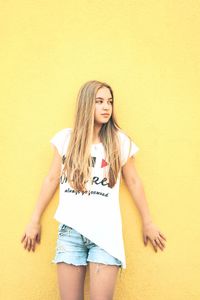 Beautiful young woman standing against yellow wall