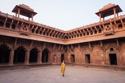 Ethnic asian woman looking away in yellow dress standing in aged arched agra fort in uttar pradesh, india