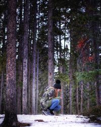 Side view of young man sitting on tree trunk in forest