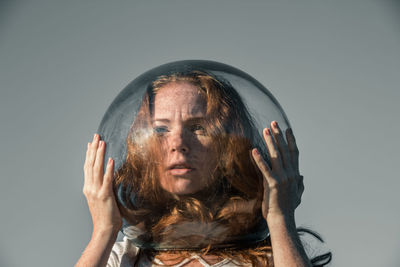 Thoughtful young woman wearing glass helmet in head against gray background