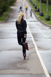 Rear view full length of woman inline skating on wet road