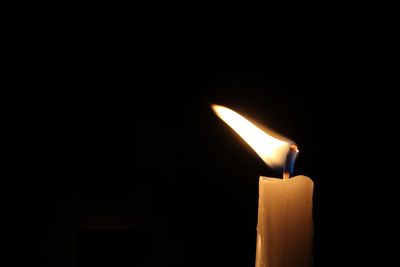 Close-up of burning candle against black background