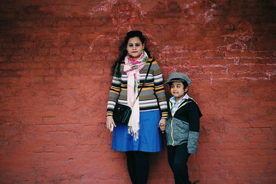 Portrait of mother with son standing against brick wall