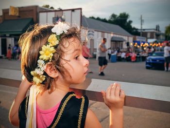 Rear view of curious girl wearing flowers by railing in city