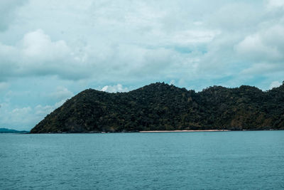 Scenic view of sea by mountain against sky