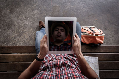 Low section of man using digital tablet while sitting on bench