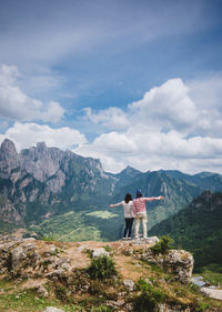 Rear view of friends standing on rock with arms outstretched against mountains