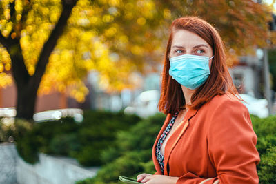 Beautiful woman wearing mask looking away while standing outdoors