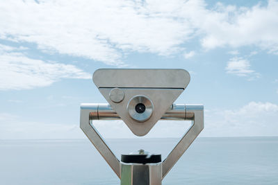 Close-up of coin-operated binoculars by sea against sky